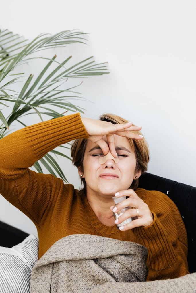 Woman on couch holding nose, hinting at bad smell or discomfort. Indoor cozy setting.