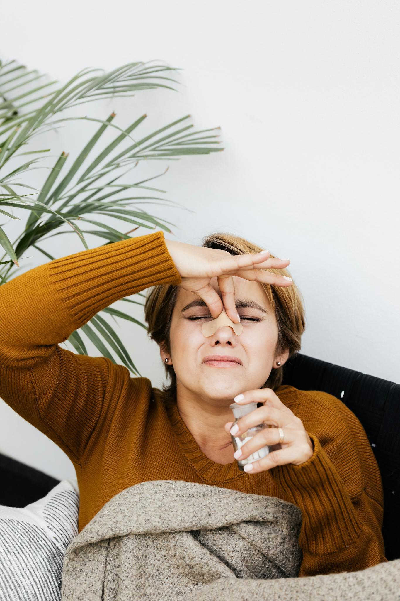 Woman on couch holding nose, hinting at bad smell or discomfort. Indoor cozy setting.